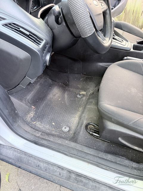 Passenger footwell of a Ford Focus before cleaning, debris across dark carpet
